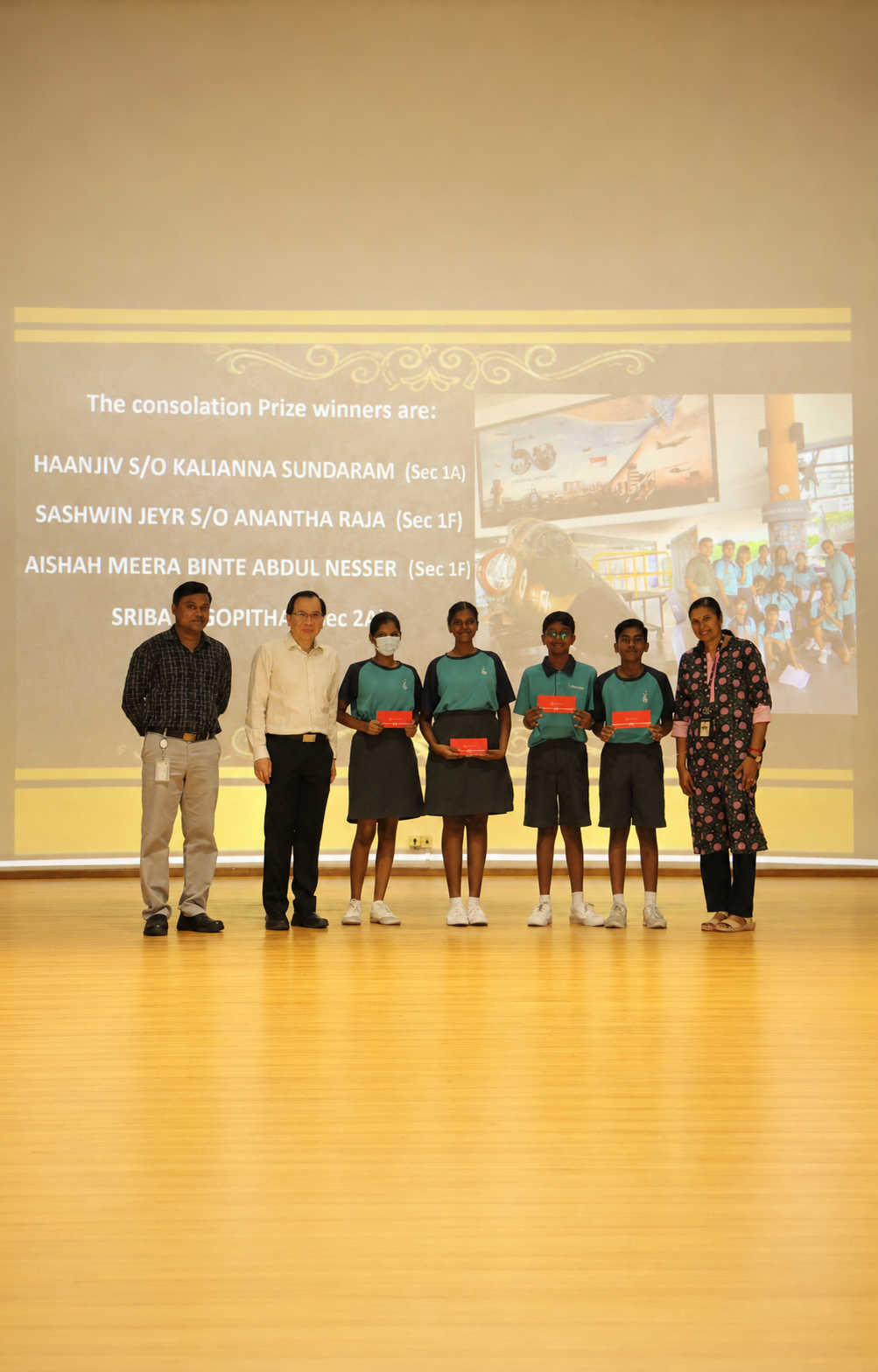 4 students and 3 teachers stand on stage with prizes